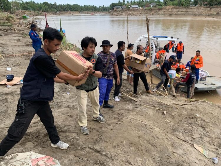Tim gabungan dari BPBD, BNPB, dan relawan di bergotong royong mengangkut logistik bantuan ke perahu yang ingin diantar menyeberang di Jembatan Kutablang, Bireuen. Minggu (14/12).